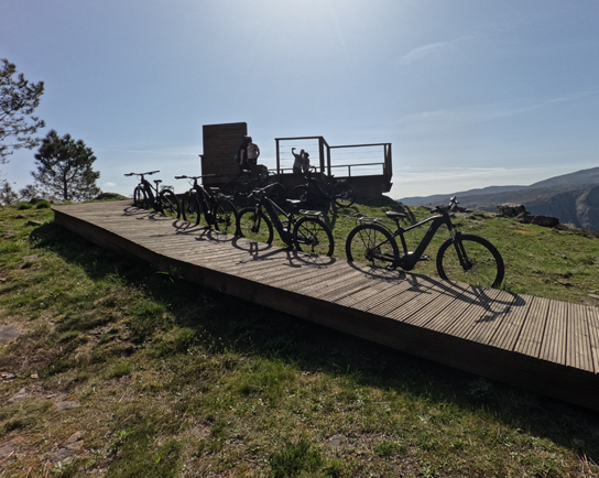 E-bikes alineadas en una pasarela de madera frente a un mirador de la Ribeira Sacra, listas para la ruta en bicicleta.