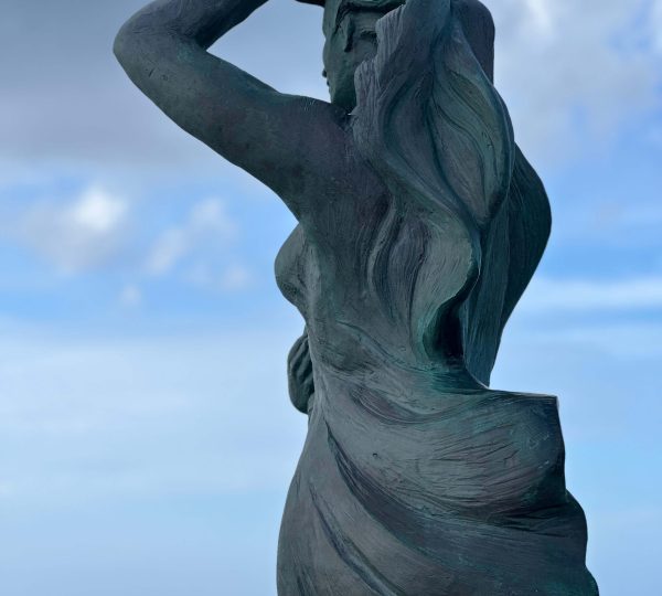 Detalle de la escultura A Espera de Laxe con el cielo y el mar al fondo