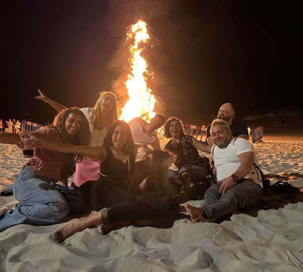 Grupo de residentes de un coliving reunidos alrededor de una hoguera en la playa